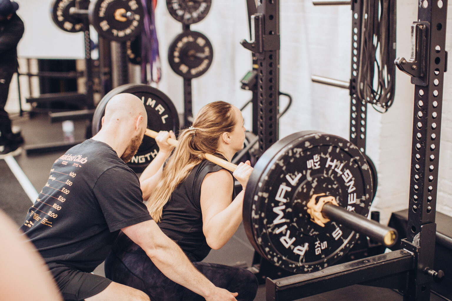 A coach guiding a member through a heavy squat