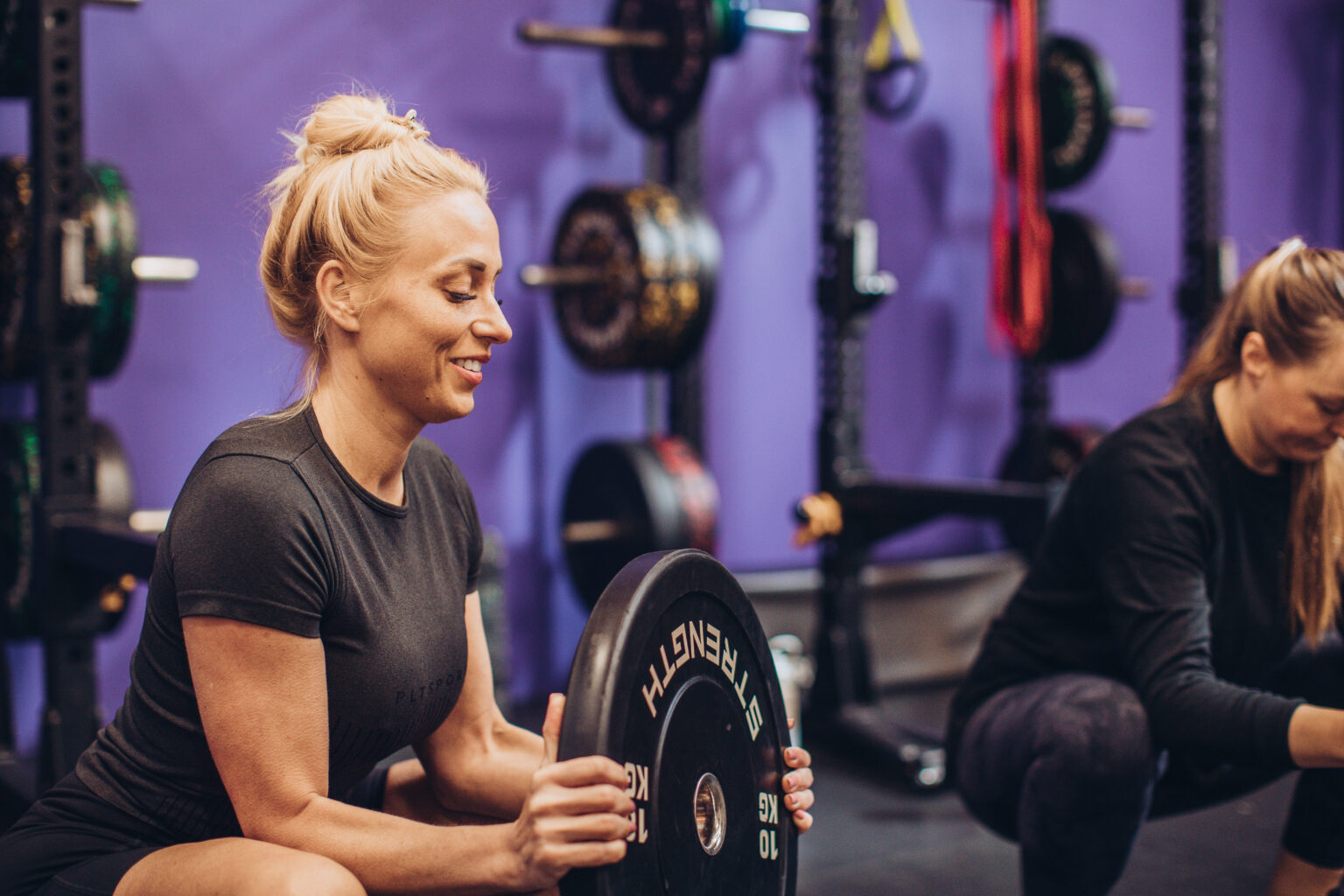 Two members loading plates and smiling during a strength session